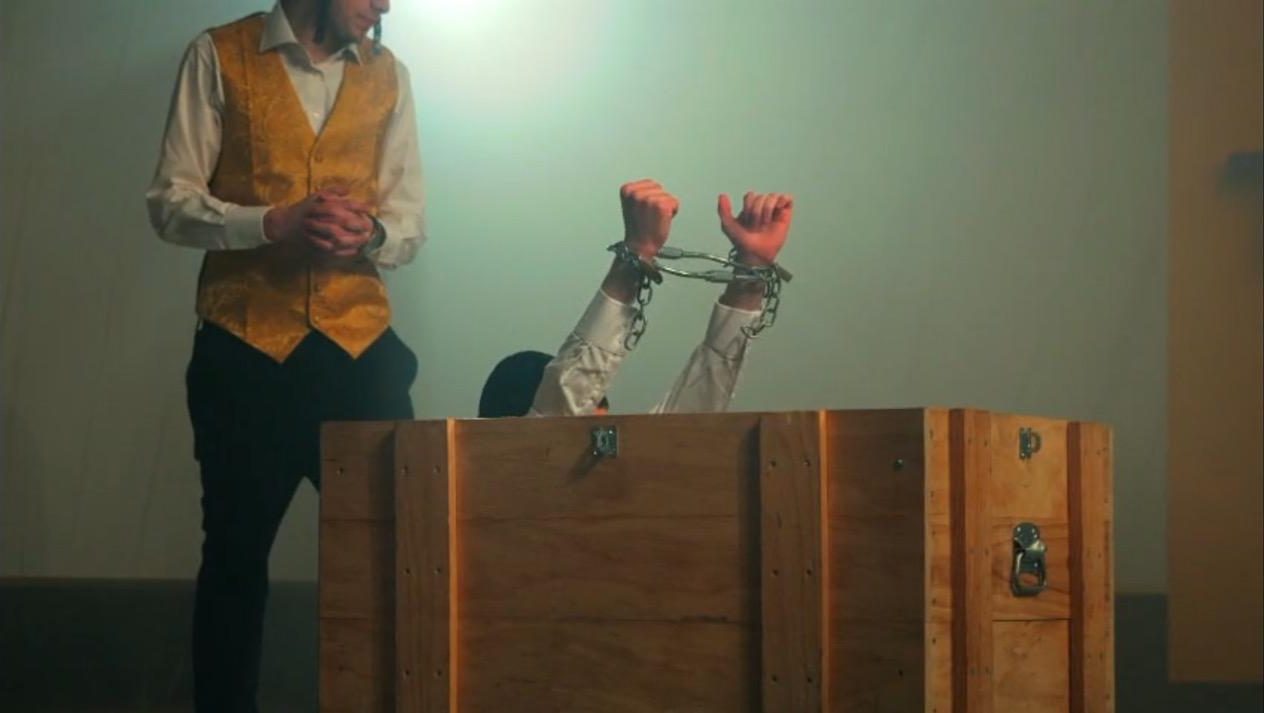 An escape routine: handcuffed hands rising out of a wooden crate on stage